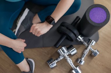 Kadın spor salonunda spor yaparken takip cihazını kontrol ediyor.