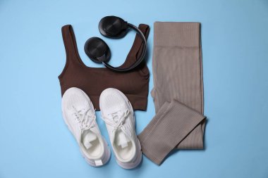 Spor kıyafetleri, kulaklıklar ve açık mavi arka planda spor ayakkabıları, düz yatış.