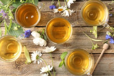Cam bardaklarda Aromatik bitki çayı, çiçekler ve yeşil yapraklar ahşap masada, düz uzanmış