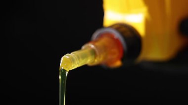 Siyah arka plana sarı teneke kutudan motor yağı dökülüyor.