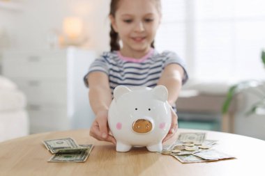 İçerideki masada kumbarası ve cep harçlığı olan kız, seçici odaklı.