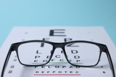 Açık mavi arkaplanda gözlük ve görüş testi grafiği, yakın plan