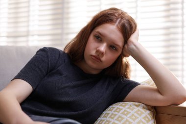 Evdeki kanepede oturan üzgün genç kız.