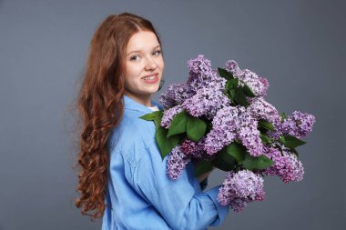 Gri arka planda leylak çiçekleri olan gülümseyen genç kız portresi