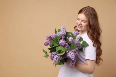 Bej arka planda bir demet leylak çiçeğiyle gülümseyen genç kız. Metin için boşluk