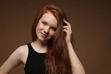 Kahverengi arka planda sağlıklı dalgalı saçlı güzel bir genç kızın portresi.