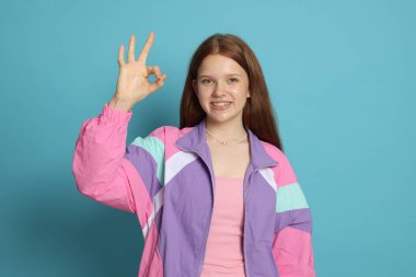 Genç kız açık mavi arka planda iyi bir jest gösteriyor.
