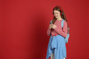 Akıllı telefonlu genç kız kırmızı arka planda müzik dinliyor. Metin için boşluk