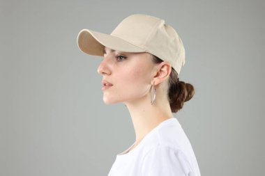 Gri arka planda şık beyzbol şapkalı güzel kadın, yakın plan.