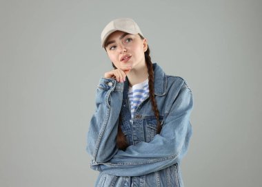 Gri arka planda şık beyzbol şapkalı düşünceli bir kadın.