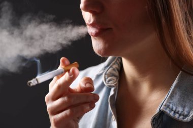 Arka planda sigara içen tişörtlü bir kadın, yakın plan. Kötü alışkanlık.