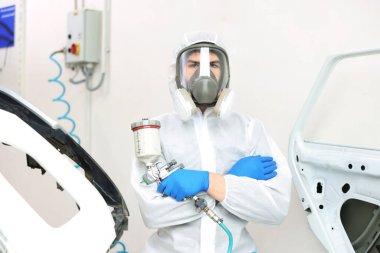 Tamirhanede sprey boya tabancası ve arabası olan bir işçi.