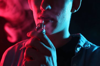 Siyah arka planda neon lambalarda elektronik sigara içen adam, yakın plan