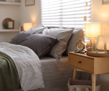 Yumuşak çarşaflı, komodinli ve lambalı rahat bir yatak. Ev tekstili