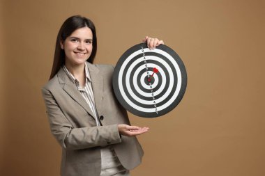 Hedef alınıyor. Dart tahtası ve bej arka planda oku olan gülümseyen iş kadını.