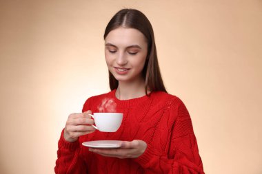 Bej renkli arka planda bir fincan kahveyle gülümseyen kadın