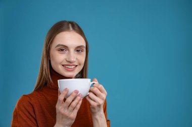 Açık mavi arka planda bir fincan kahveyle gülümseyen kadın. Metin için boşluk