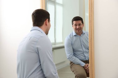 Yakışıklı adam aynada kendine bakıyor.