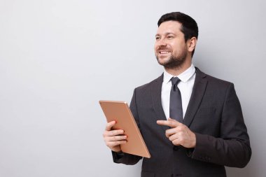 Açık gri arka planda tableti olan gülümseyen bir işadamı. Metin için boşluk