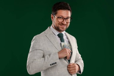 Mutlu açgözlü bankacı yeşil arka planda takım elbisenin iç cebine para saklıyor.