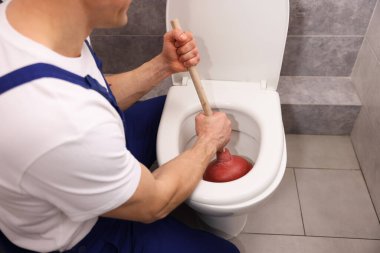 Tesisatçı tuvalet tıkanıklığını açıyor, içeride pompa var, yakın plan.