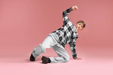 Kulaklıklı, şık elbiseli, pembe arka planda dans eden bir çocuk.