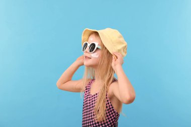 Yüzünde güneş kremiyle gülümseyen küçük kız açık mavi arka planda.