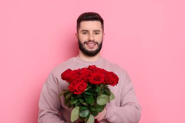 Pembe arka planda kırmızı güller açan mutlu bir adam.