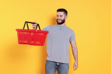 Turuncu arka planda boş alışveriş sepeti olan adam.