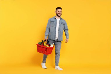 Turuncu arka planda ürünlerle dolu alışveriş sepeti olan bir adam.