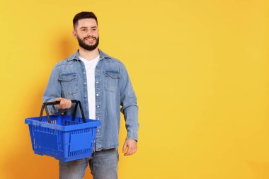 Turuncu arka planda boş alışveriş sepeti olan adam, mesaj için boşluk