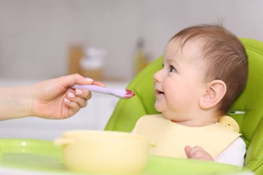 Anne bebeğini sandalyeyle besliyor, yakın plan.