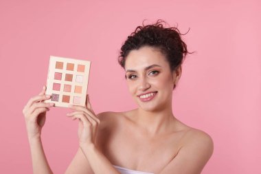 Pembe arka planda göz farı paleti olan gülümseyen kadın.