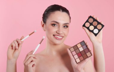 Göz farı paletleri, fırçalar ve pembe arka planda gülümseyen bir kadın olan makyaj sanatçısı.