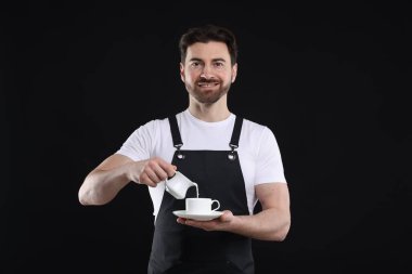 Gülümseyen barista siyah arka planda kahve yapıyor.