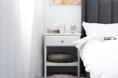 Yatağın yanında alarm saati ve dekorasyonu olan komodinin yanında.