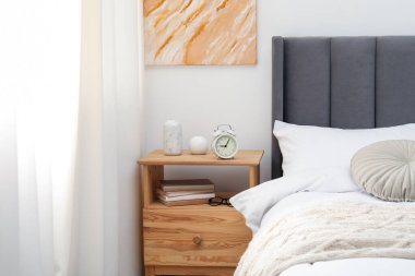 Yatağın yanında alarm saati ve dekorasyonu olan komodinin yanında.