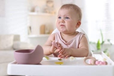 Evdeki beslenme sandalyesinde çatalla yemek yiyen şirin bir bebek.