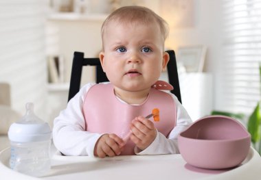 Evdeki beslenme sandalyesinde çatalla yemek yiyen şirin bir bebek.