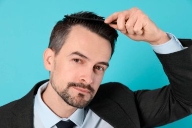 Yakışıklı adam saçlarını açık mavi arka planda tarak ile tarıyor.