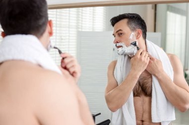 Yakışıklı adam evde aynanın yanında tıraş oluyor.