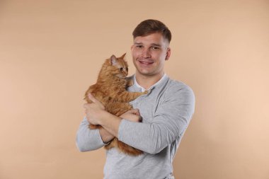 Bej arka planda sevimli kızıl kedisi olan adam.