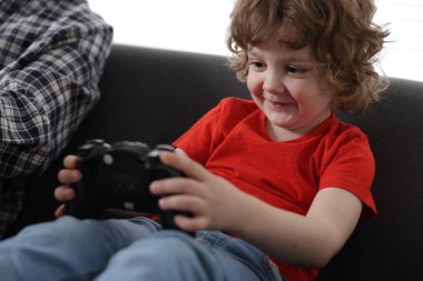 Küçük çocuk ve babası evde oyun kontrolörüyle oynuyorlar.