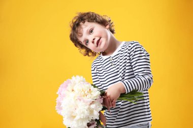 Sarı arka planda bir buket güzel şakayığı olan sevimli küçük bir çocuk.