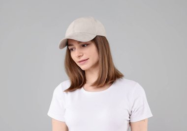 Açık gri arka planda bej renkli beysbol şapkası takan genç bir kadın.