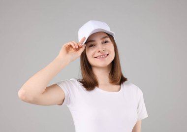 Açık gri arka planda şık beyaz beyzbol şapkası takan genç bir kadın.