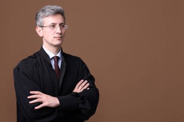 Kahverengi arka planda çapraz kolları olan mahkeme elbiseli bir yargıç. Metin için boşluk