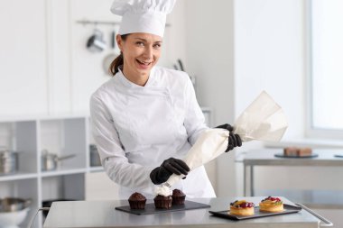 Şekerci mutfakta kremayla kek süslüyor.