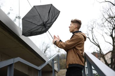 Kırık şemsiyeli bir adam açık havada yağmur altında rüzgarla savaşıyor.