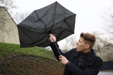 Kırık şemsiyeli bir adam açık havada yağmur altında rüzgarla savaşıyor.